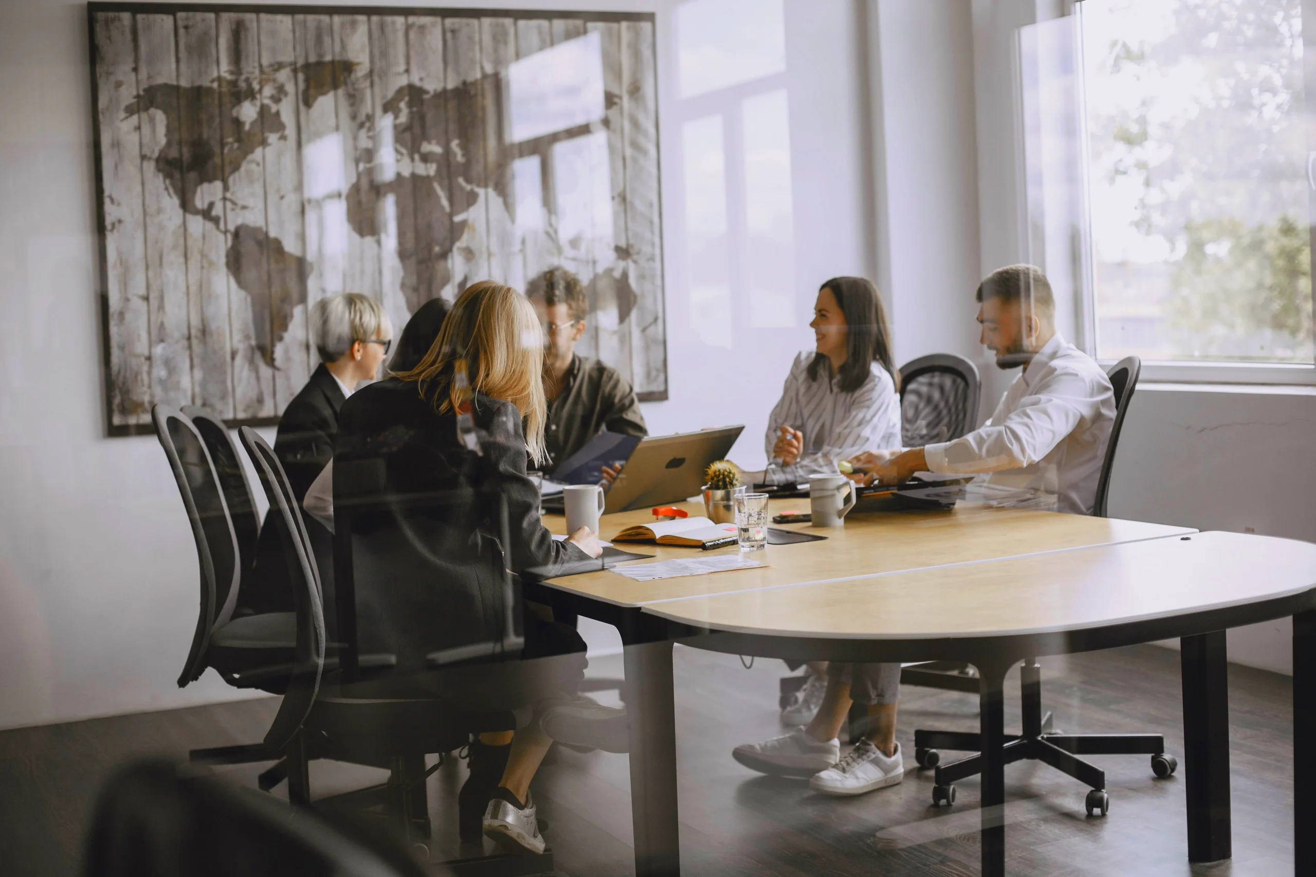 Five colleagues in discussion around a table in a bright meeting room.